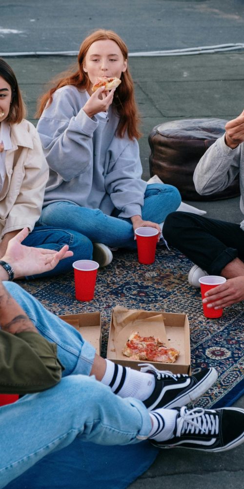 A group of friends enjoying pizza on a rooftop, relaxed vibes and summer evening.